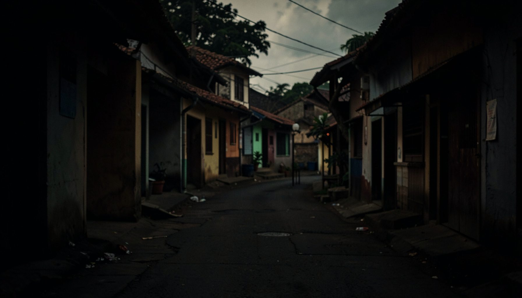 A dark, low-key photograph of a quiet street scene in a provincial Philippine town, deep shadows and muted earth tones, early morning light
