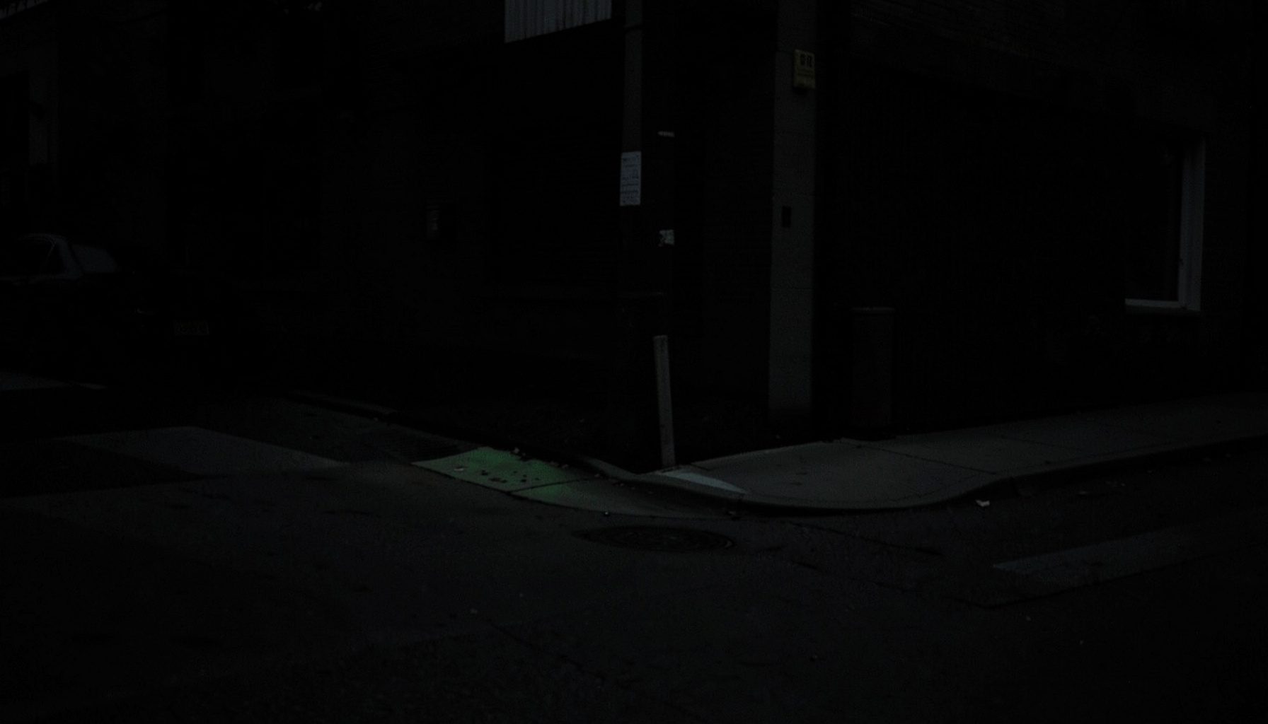 A dim, low-key photograph of a quiet street corner at dusk, deep shadows and muted gray tones, calm and understated mood